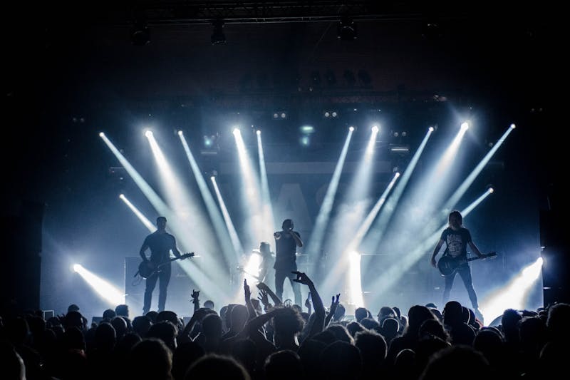 Bright stage lighting illuminating a night-time music festival crowd.